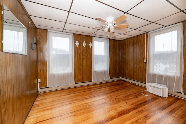 spare room featuring wood walls, ceiling fan, light hardwood / wood-style floors, a wall mounted air conditioner, and a paneled ceiling