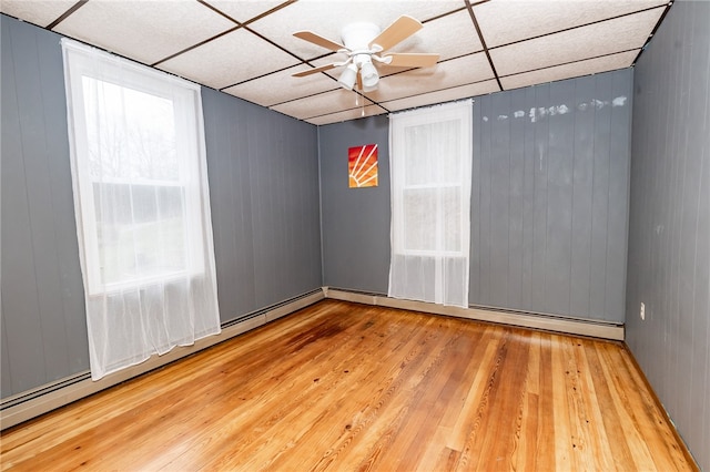 spare room with a drop ceiling, a baseboard heating unit, light hardwood / wood-style flooring, and ceiling fan