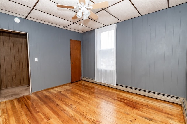 spare room featuring a drop ceiling, baseboard heating, light hardwood / wood-style floors, and ceiling fan