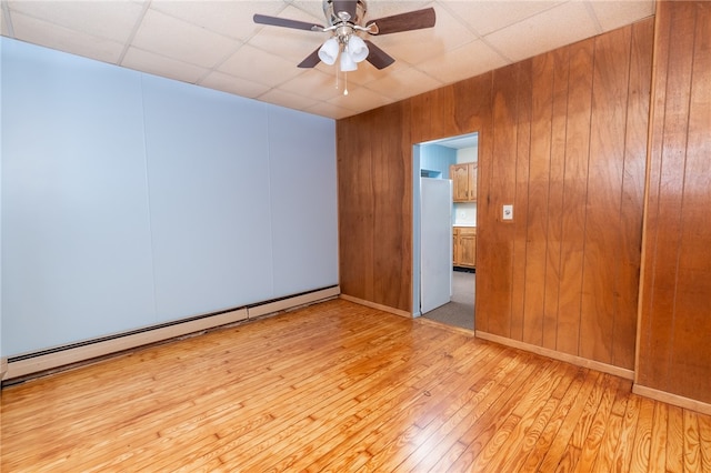 empty room with a baseboard radiator, ceiling fan, light wood-type flooring, and a paneled ceiling