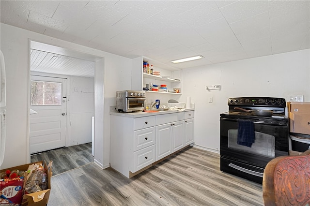 kitchen with black electric range oven, sink, white cabinetry, and light hardwood / wood-style flooring