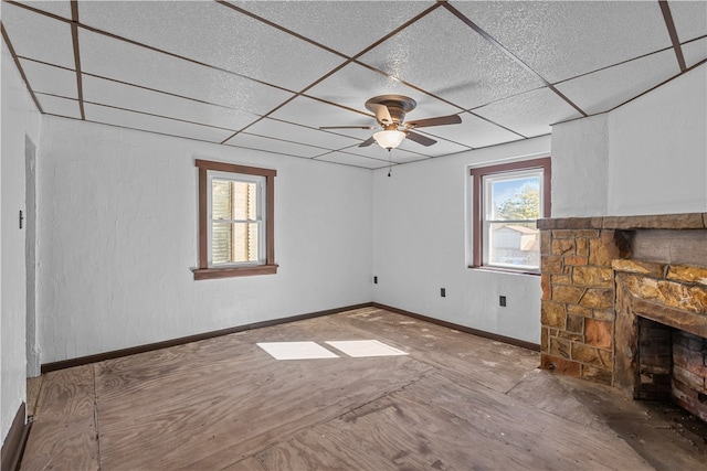 unfurnished living room featuring a paneled ceiling, ceiling fan, and a fireplace