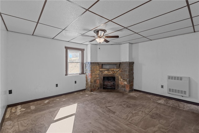 unfurnished living room featuring ceiling fan, a paneled ceiling, and a stone fireplace