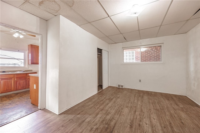 basement with ceiling fan, a paneled ceiling, and wood-type flooring