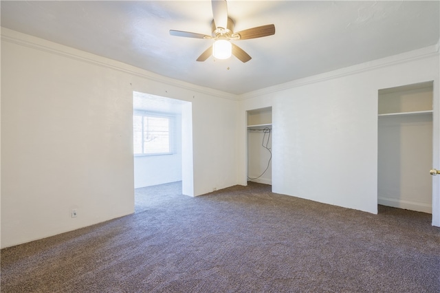 unfurnished bedroom featuring ceiling fan, dark carpet, two closets, and ornamental molding