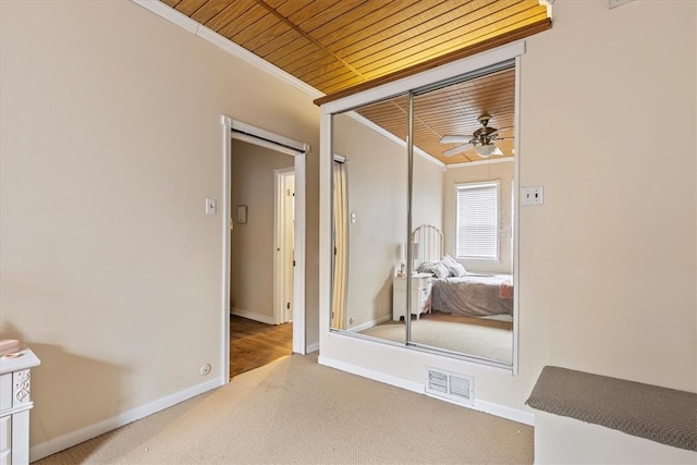 unfurnished bedroom featuring a closet, wood ceiling, light carpet, and crown molding