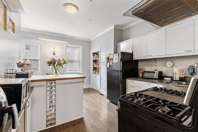 kitchen with black refrigerator, white cabinets, custom exhaust hood, light hardwood / wood-style flooring, and ornamental molding