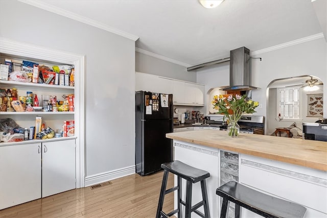 kitchen with ceiling fan, stainless steel range, island range hood, white cabinetry, and black fridge