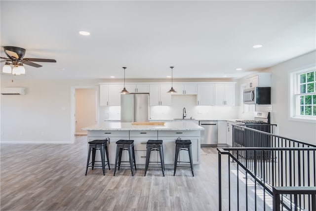 kitchen with appliances with stainless steel finishes, white cabinets, sink, a wall mounted AC, and light hardwood / wood-style floors