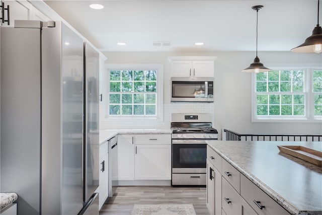 kitchen featuring white cabinetry, hanging light fixtures, light wood-type flooring, appliances with stainless steel finishes, and backsplash