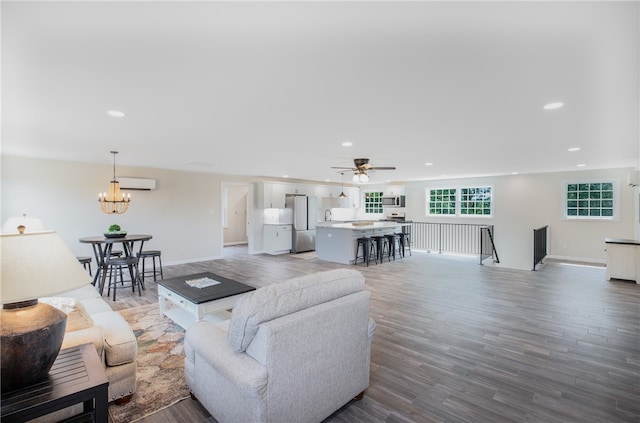 living room featuring hardwood / wood-style flooring, ceiling fan with notable chandelier, and an AC wall unit