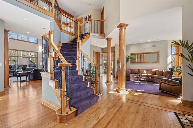 stairway featuring hardwood / wood-style floors, a towering ceiling, and decorative columns