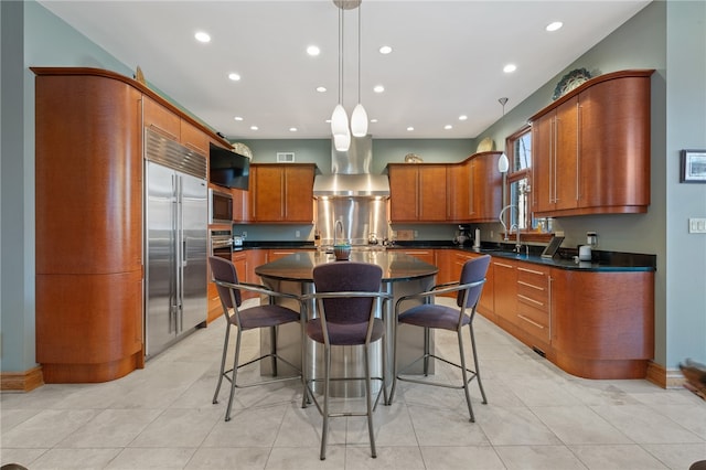 kitchen featuring wall chimney exhaust hood, a kitchen island, built in appliances, and decorative light fixtures