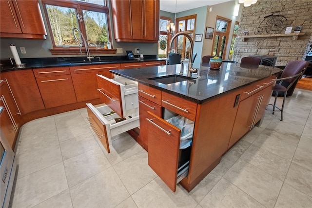 kitchen featuring hanging light fixtures, a stone fireplace, sink, and an island with sink