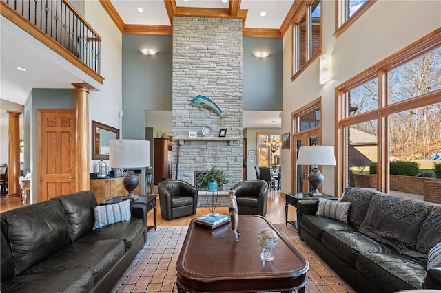 living room featuring a stone fireplace, a towering ceiling, ornate columns, and crown molding