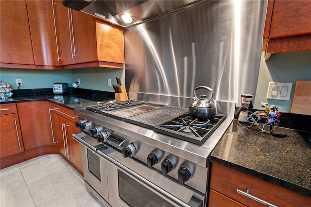 kitchen featuring dark stone counters, light tile patterned flooring, and range with two ovens