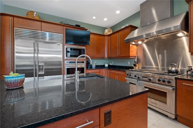 kitchen featuring light tile patterned floors, sink, wall chimney range hood, built in appliances, and dark stone countertops