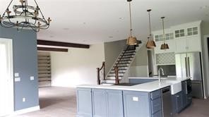 kitchen with blue cabinetry, decorative light fixtures, an island with sink, a chandelier, and stainless steel dishwasher