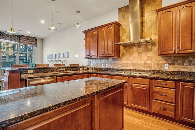 kitchen featuring wall chimney exhaust hood, stainless steel appliances, sink, dark stone counters, and light hardwood / wood-style floors