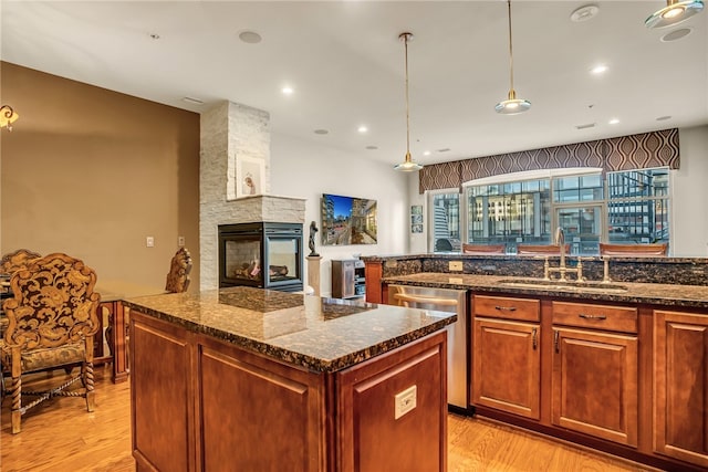 kitchen with a fireplace, sink, dishwasher, decorative light fixtures, and light hardwood / wood-style flooring