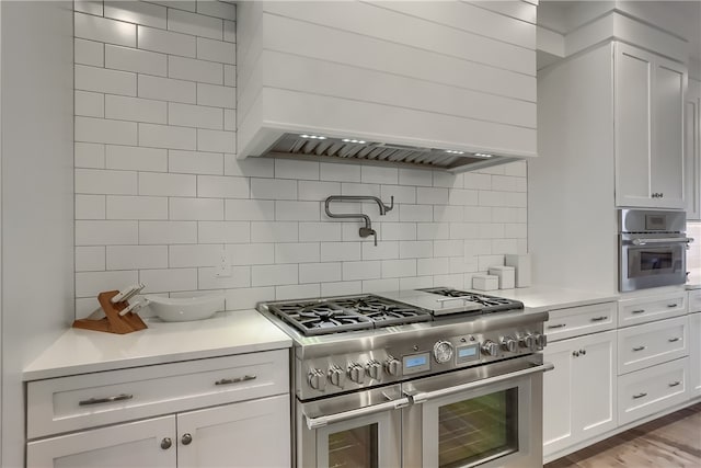 kitchen featuring light hardwood / wood-style floors, white cabinetry, backsplash, stainless steel appliances, and premium range hood