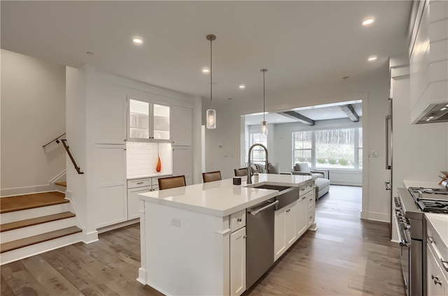 kitchen with dark hardwood / wood-style floors, sink, white cabinets, stainless steel appliances, and a center island with sink