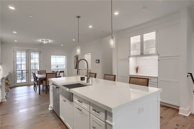 kitchen with light hardwood / wood-style floors, tasteful backsplash, white cabinets, a center island with sink, and sink