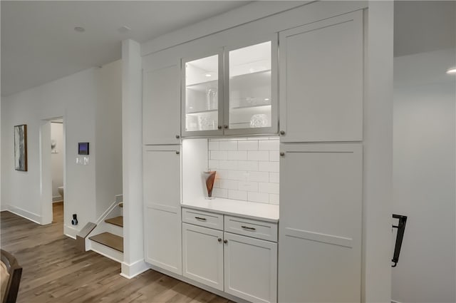 bar featuring light wood-type flooring, tasteful backsplash, and white cabinets