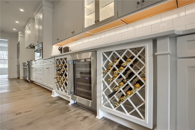 bar with light wood-type flooring, wine cooler, tasteful backsplash, white cabinetry, and appliances with stainless steel finishes