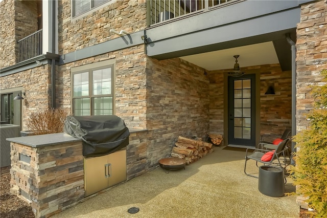 property entrance with cooling unit, a balcony, a patio, and exterior kitchen