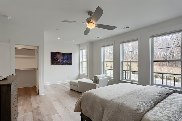 bedroom with light hardwood / wood-style floors, ceiling fan, a walk in closet, and a closet