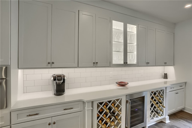 bar featuring wood-type flooring, decorative backsplash, and beverage cooler