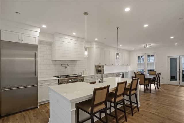 kitchen featuring white cabinetry, an island with sink, high end appliances, french doors, and dark hardwood / wood-style floors