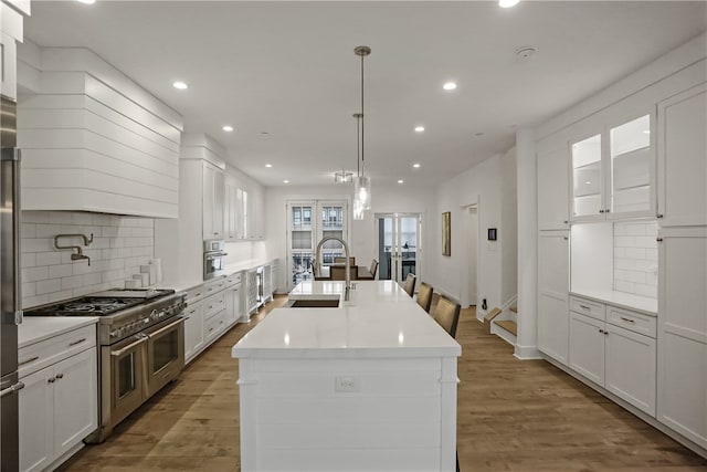 kitchen featuring decorative backsplash, white cabinets, stainless steel appliances, a kitchen island with sink, and hardwood / wood-style floors