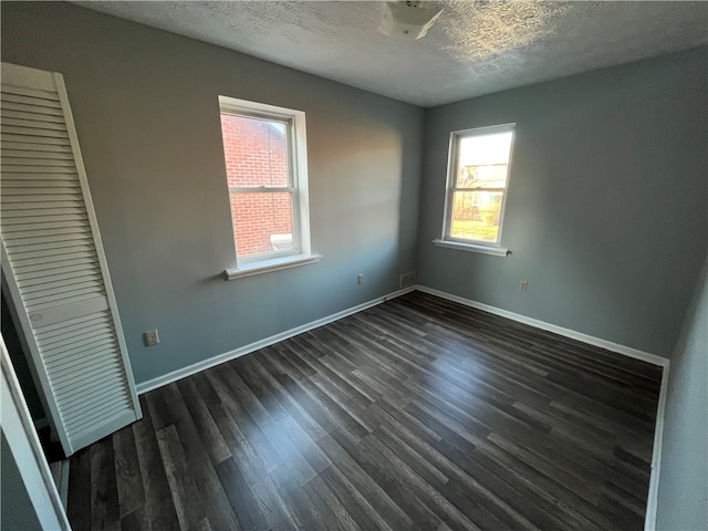 unfurnished bedroom with dark hardwood / wood-style flooring, multiple windows, a textured ceiling, and a closet