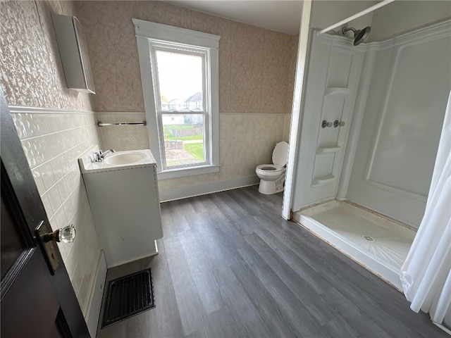 bathroom with wood-type flooring, toilet, walk in shower, tile walls, and vanity