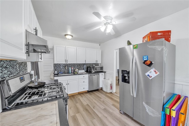 kitchen with ceiling fan, appliances with stainless steel finishes, white cabinets, tasteful backsplash, and wall chimney exhaust hood