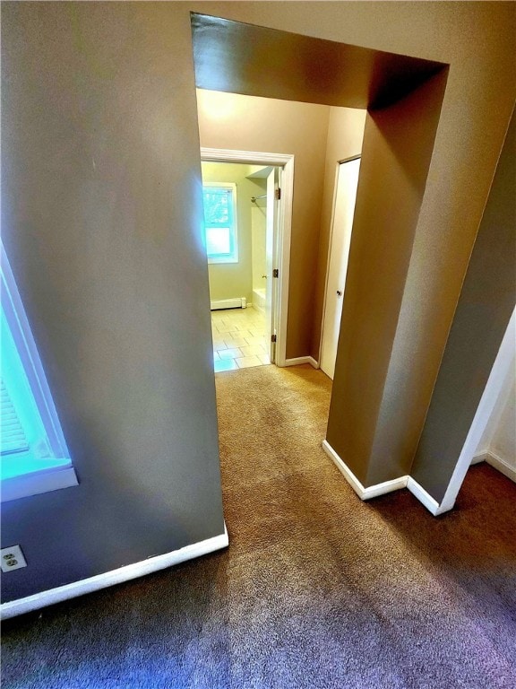 corridor with a baseboard heating unit and carpet floors