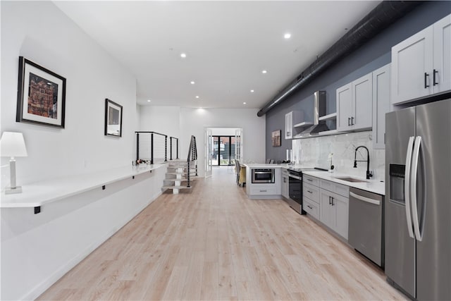 kitchen with sink, light hardwood / wood-style flooring, appliances with stainless steel finishes, and wall chimney range hood