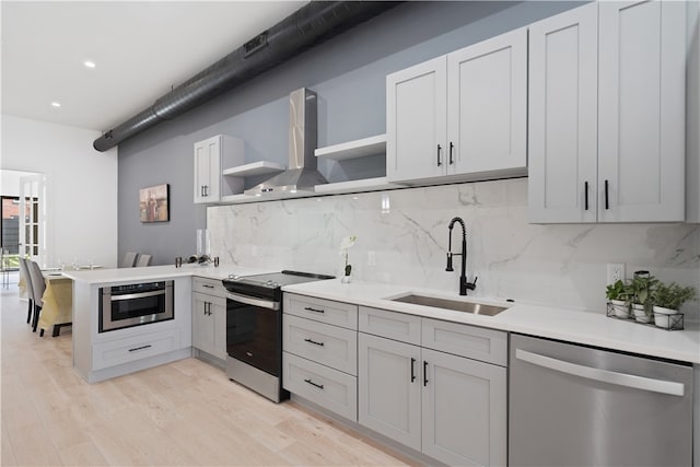 kitchen with backsplash, light hardwood / wood-style floors, sink, stainless steel appliances, and wall chimney exhaust hood