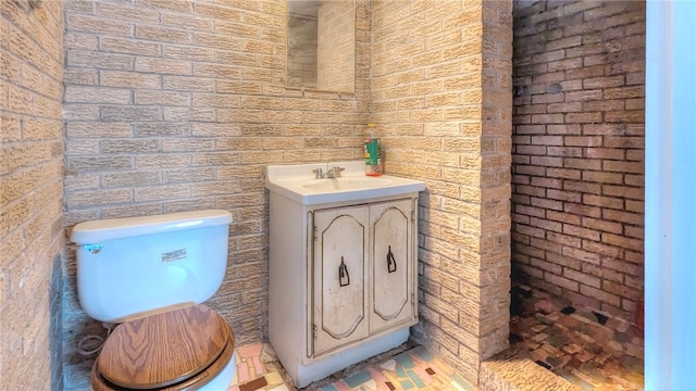 bathroom featuring brick wall, toilet, and vanity