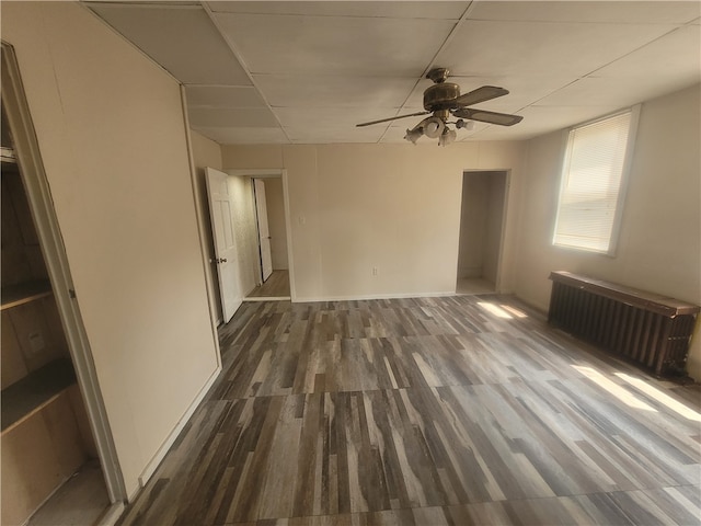 unfurnished room with ceiling fan, a drop ceiling, dark hardwood / wood-style flooring, and radiator