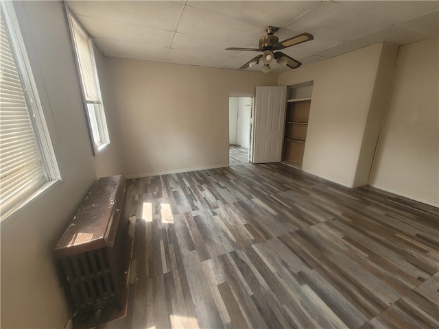 empty room with dark wood-type flooring, ceiling fan, and a drop ceiling