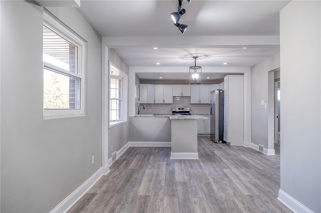 kitchen featuring hanging light fixtures, light hardwood / wood-style flooring, stainless steel refrigerator with ice dispenser, stove, and tasteful backsplash