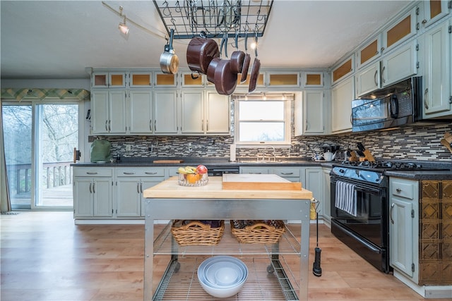 kitchen with backsplash, a wealth of natural light, black appliances, and light hardwood / wood-style floors