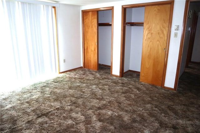 unfurnished bedroom with two closets and dark colored carpet