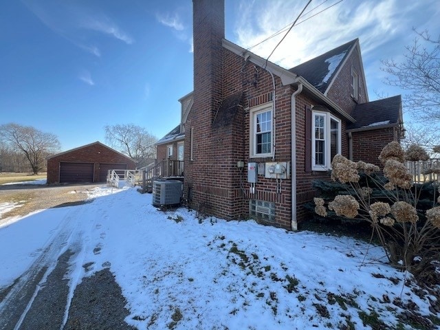 view of snowy exterior with central AC unit and a garage