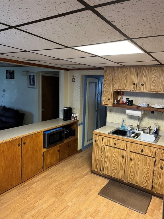 kitchen featuring sink, stainless steel microwave, a paneled ceiling, tasteful backsplash, and light wood-type flooring