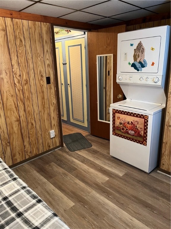 clothes washing area featuring stacked washer and clothes dryer, dark hardwood / wood-style flooring, and wood walls