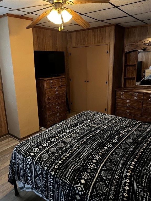 bedroom with ceiling fan, a drop ceiling, wood walls, and light hardwood / wood-style floors